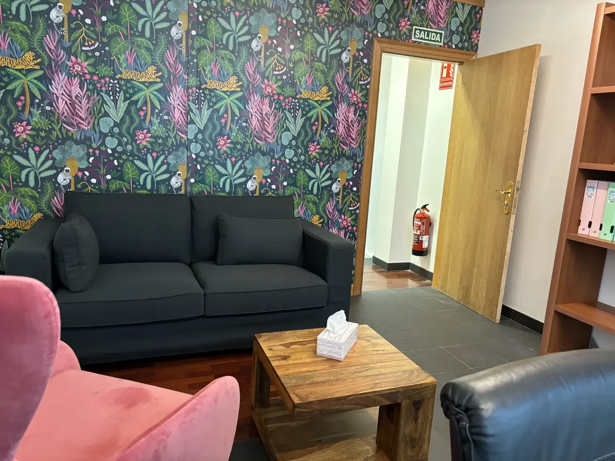 Sofá gris oscuro, mesa baja de madera con pañuelos y la puerta de salida de la consulta